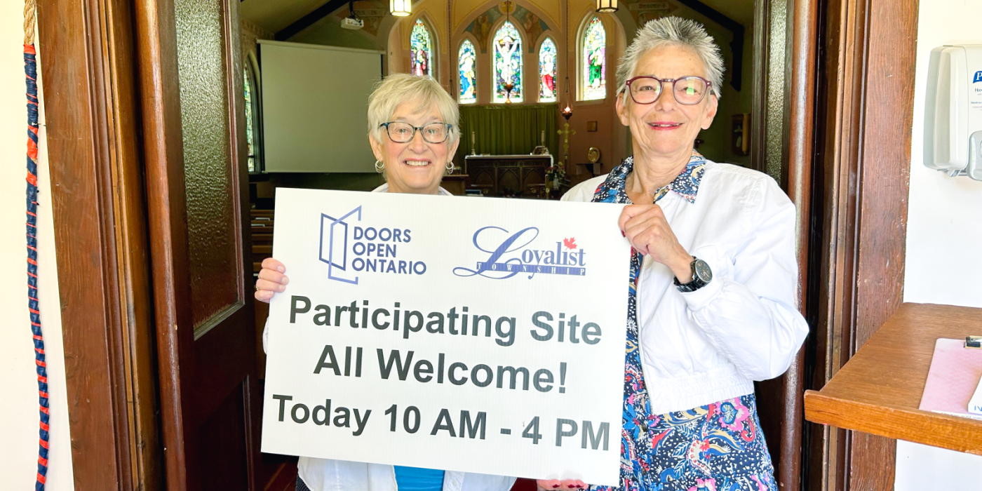 two ladies standing in front of open church door holding a sign